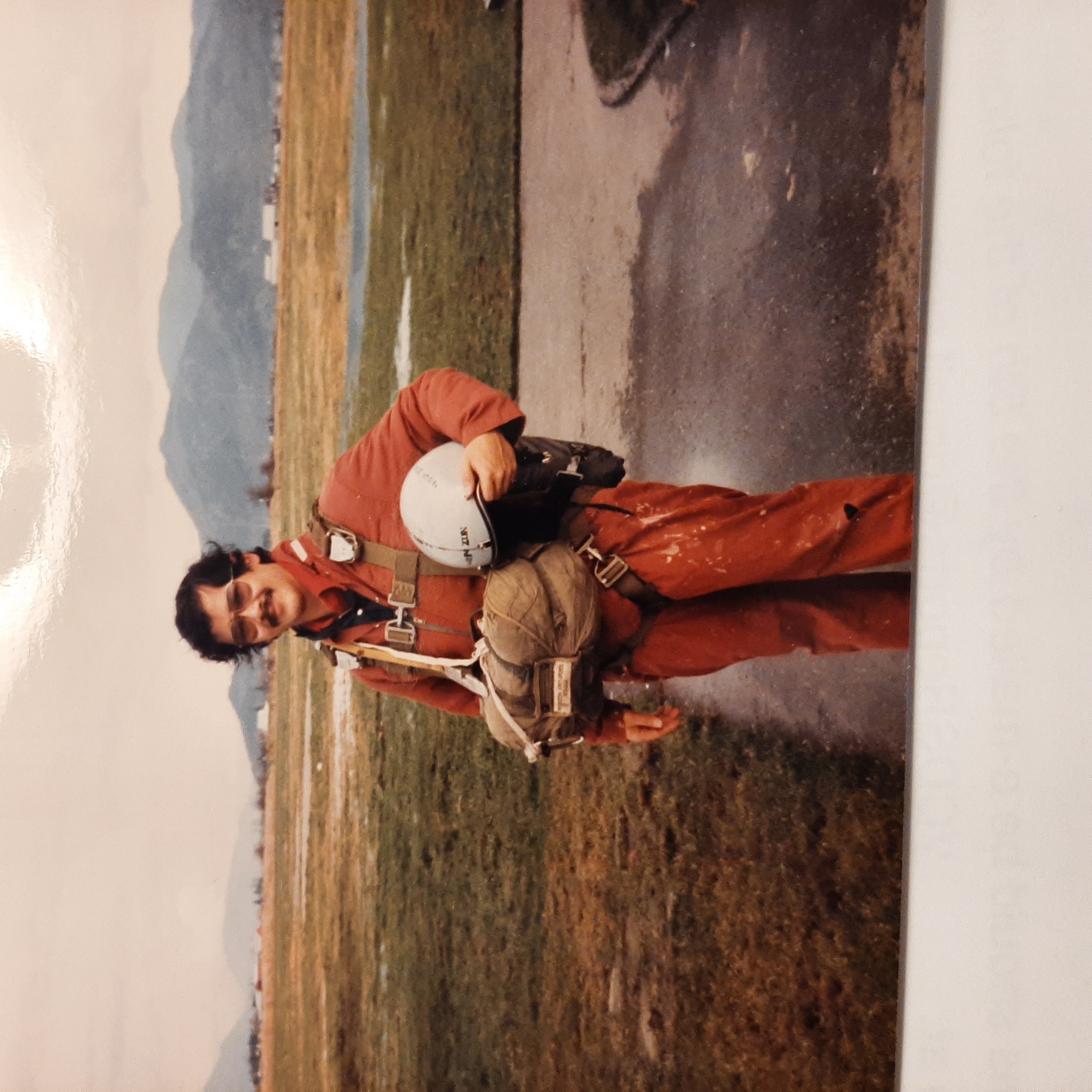 Ted Lee wearing a red jumpsuit and parachute gear after skydiving in 1982